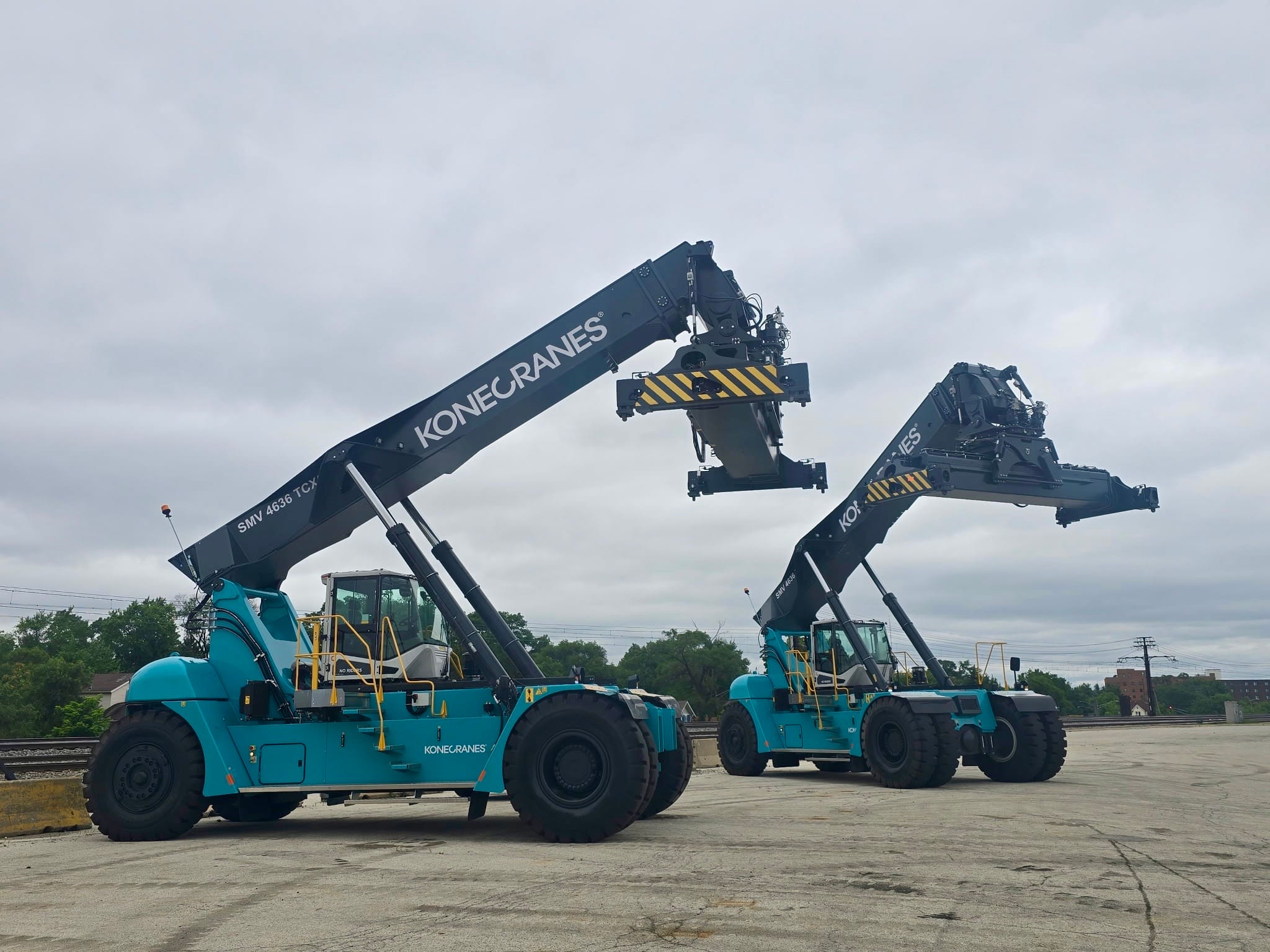 Two Konecranes reach stackers staged beside an active rail line